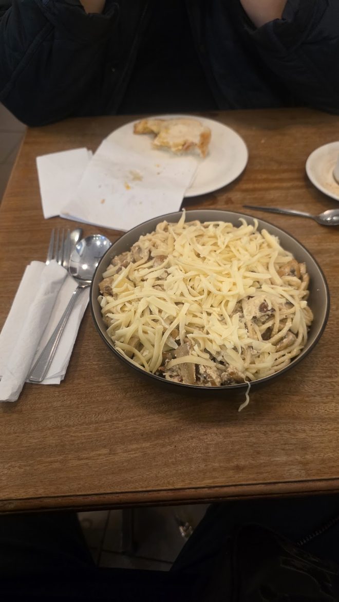 Carbonara on a dim wooden table with cutlery beside it